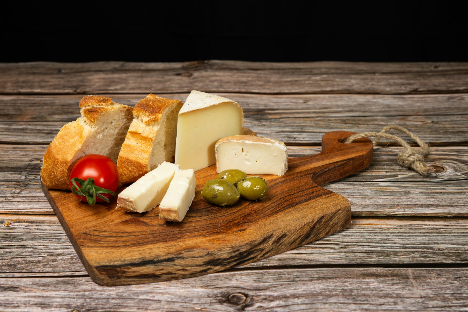 Ahşap sunum tahtasında peynir, ekmek, zeytin ve domates